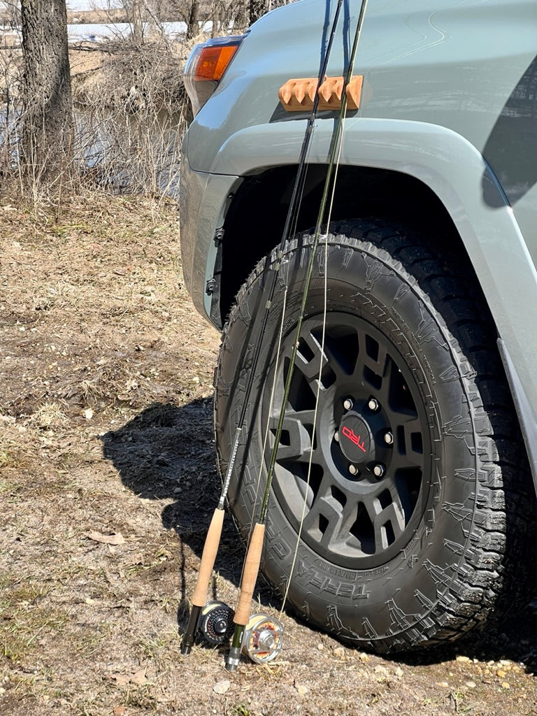 Two fishing rods leaning against a vehicle, secured by a CastHitch magnetic rod holder attached to the side of the car, providing convenient and safe rod storage for anglers during trips.
