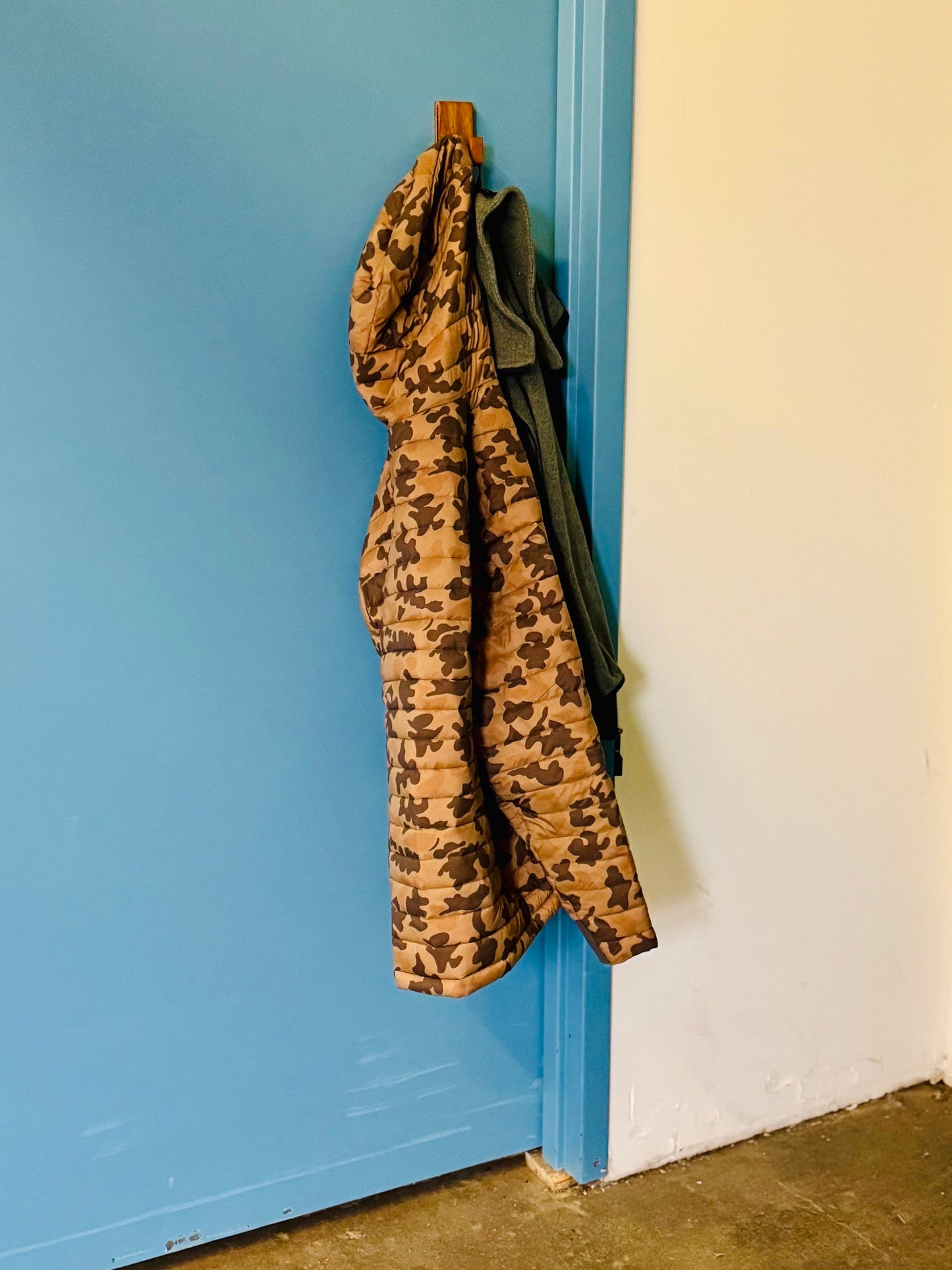 Gearhook on the back of an industrial metal door with a camouflage coat hanging from it. showcasing its versatility for alternative uses beyond fishing gear.