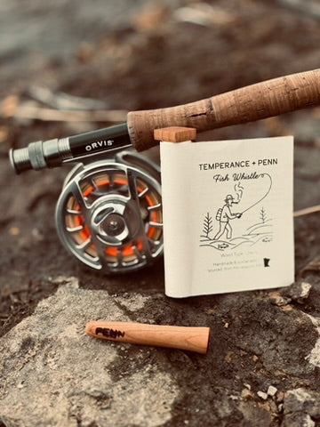 wooden pipe or chillem or onie for smoking weed next to paper packaging and a fly rod sitting on a rock